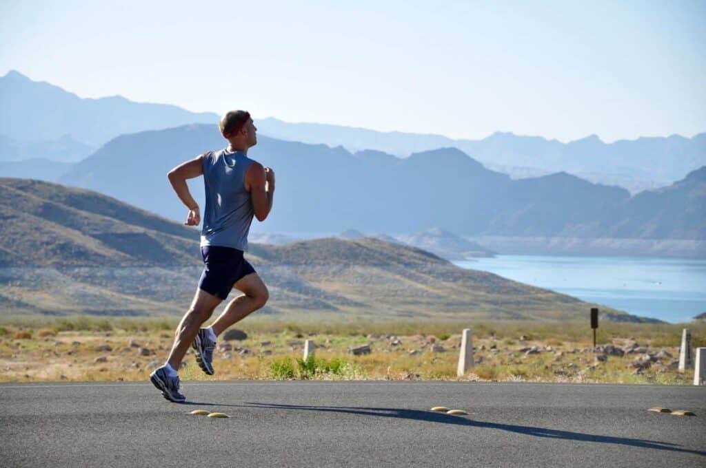 A man jogging on the road with gorgeous views of the ocean and blue mountains in the background