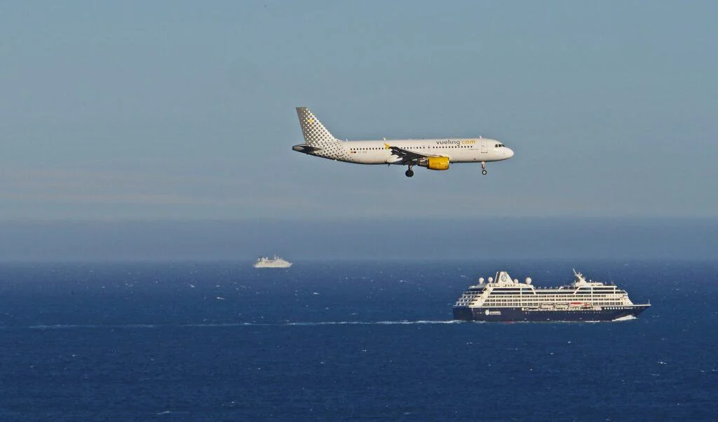 A plane lying overhead a cruise ship sailing across the ocean