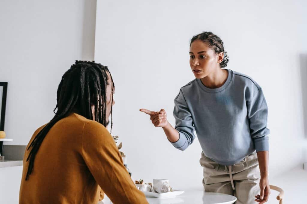 A Black couple is having heated arguments, with the wife standing and angrily pointing at her husband, seated at their dining table.