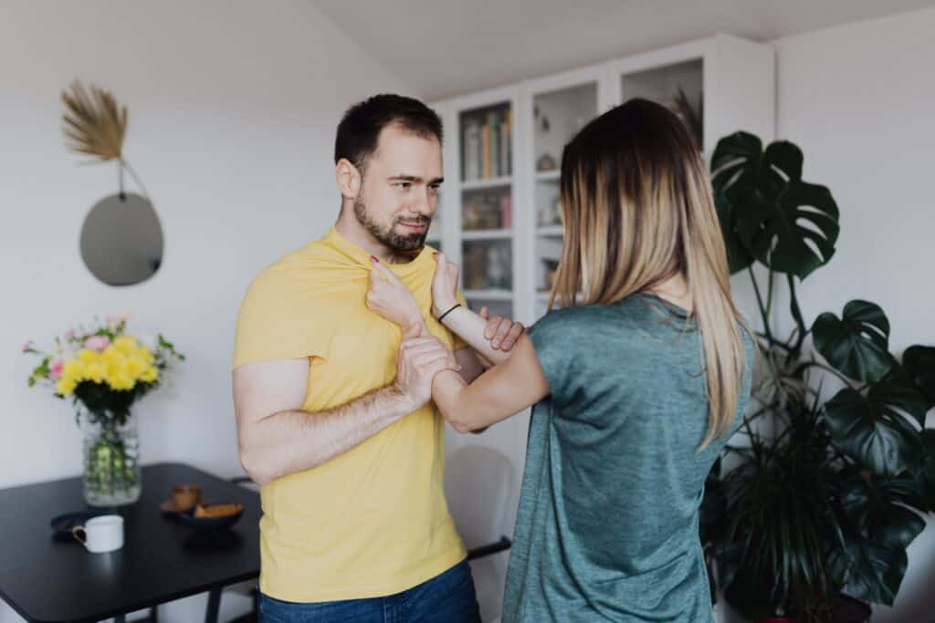 A couple that is engaged in a fight with the wife holding the husband on the collar while the husband holds her in both hands.