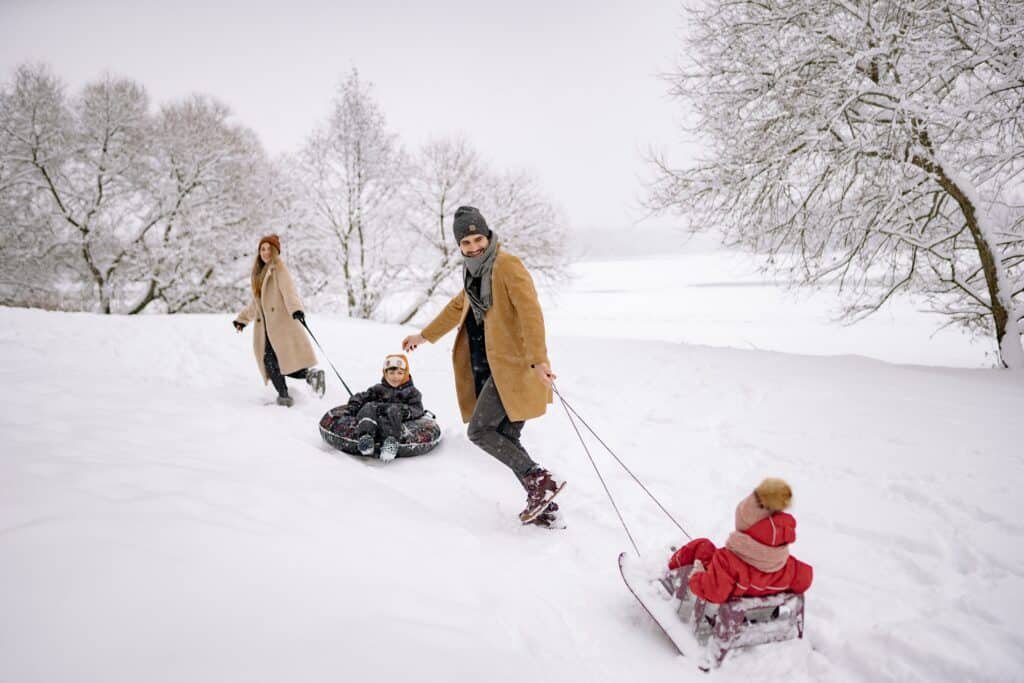 A couple enjoying quality family time with their two children whom they are pulling over snow on sledges.