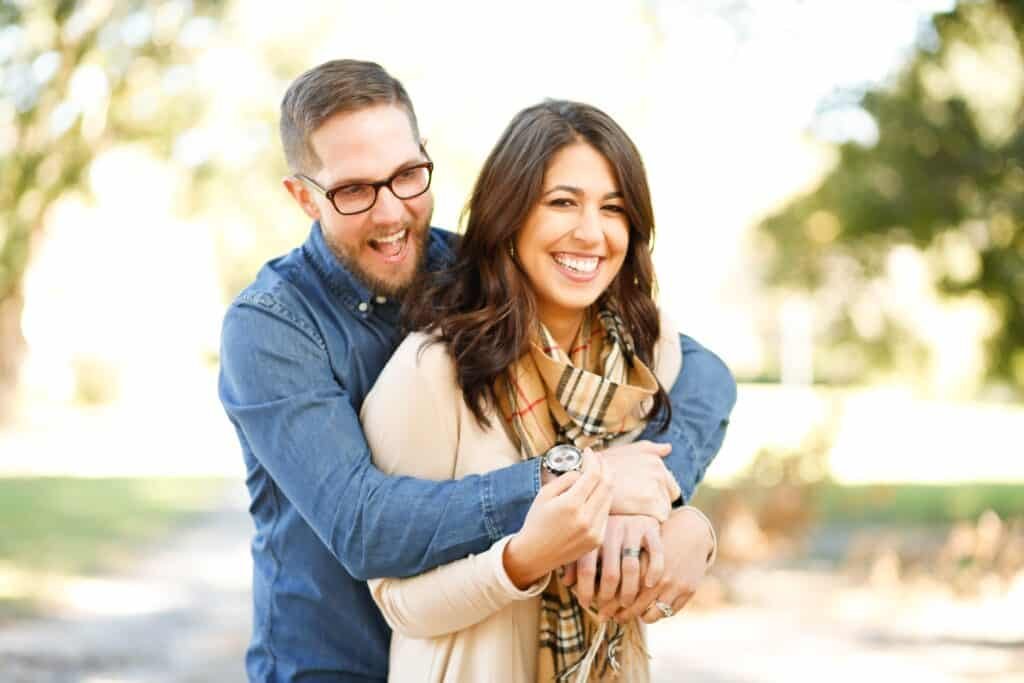 A young couple laughing while the husband is cuddling his wife from behind content that his emotional needs are being met.