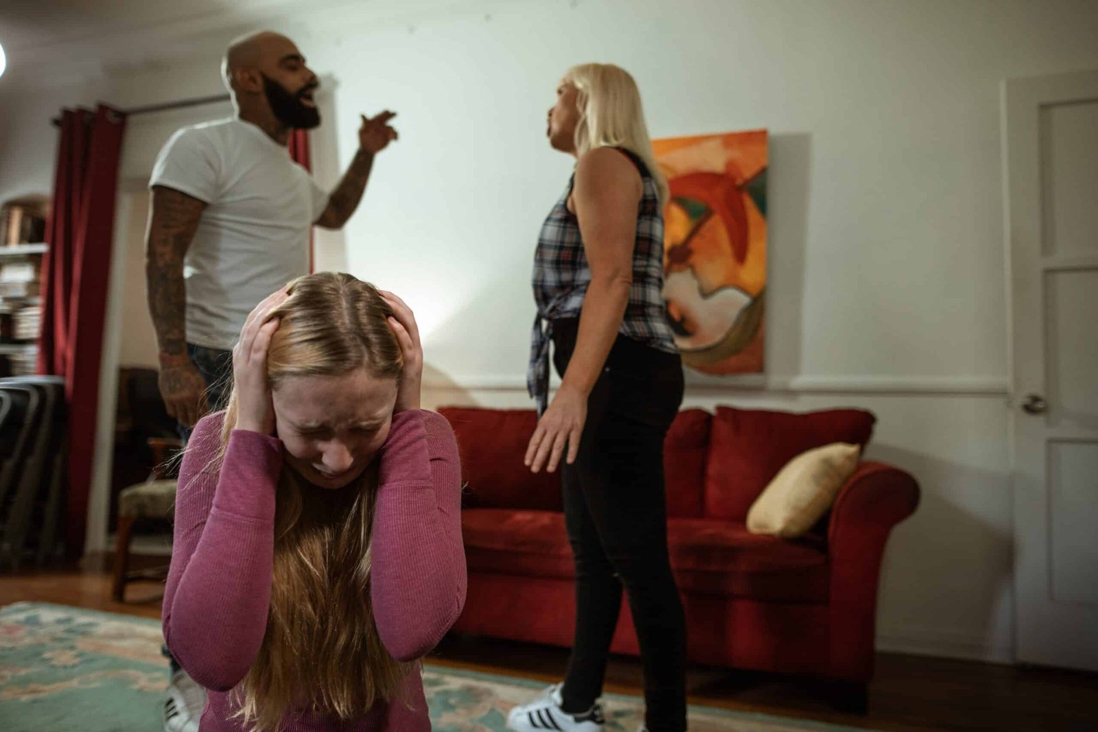 A couple is having heated, loud arguments, with the husband gesturing while their daughter is crying and covering her two ears.