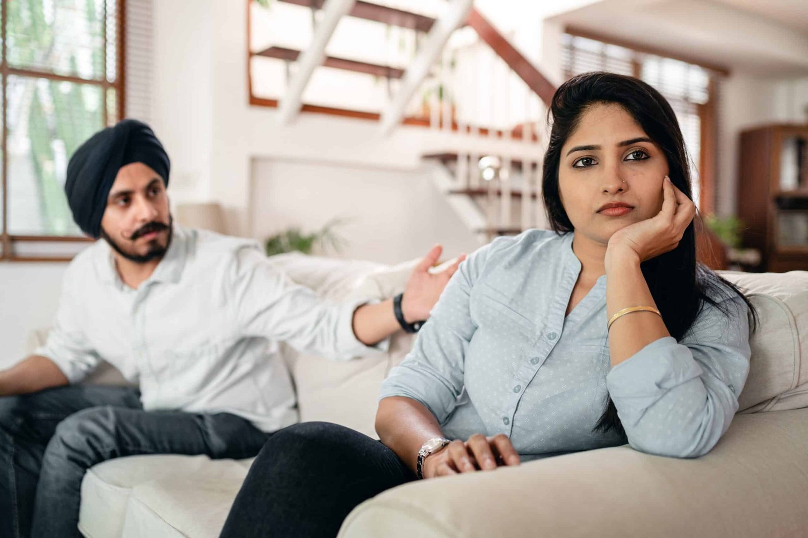 An Indian couple learning conflict resolution in marriage, seated apart from each other on a couch, the husband talking to the wife who is looking away and not paying any attention.