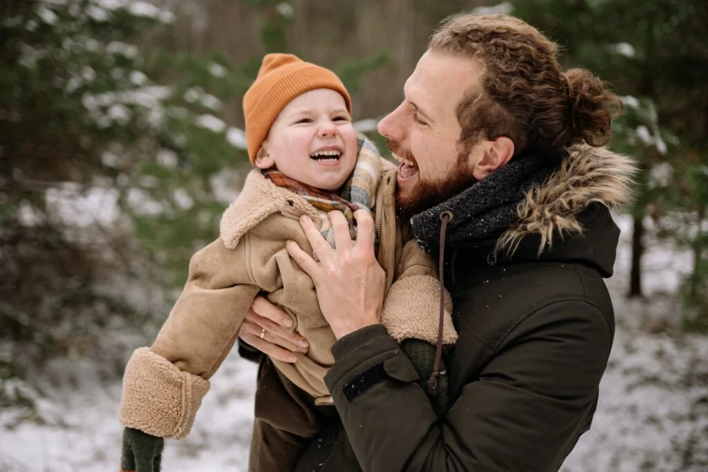 Dad and his son dressed in Winter wear in surrounded by white snow with both happy while the dad carries his son. 