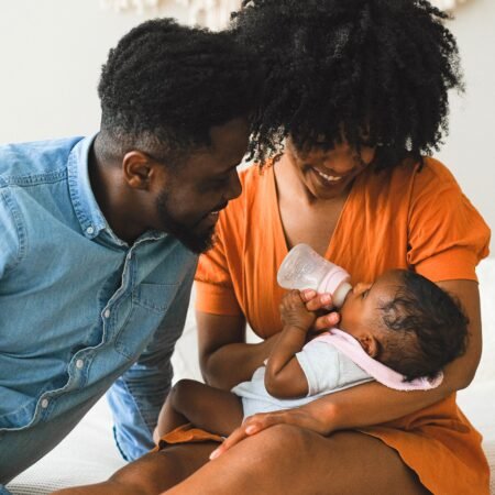 A Black couple happily bottle feeding their new baby in their recent transition to parenthood