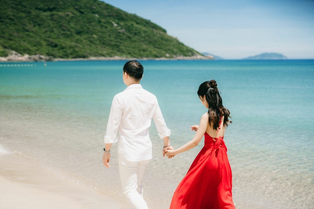 A young couple holding hands walking by the beach during the honeymoon stage of their marriage relationship.