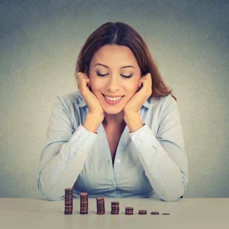 A female executive who is smiling while staring at a pile of coins as evidence she is achieving financial freedom