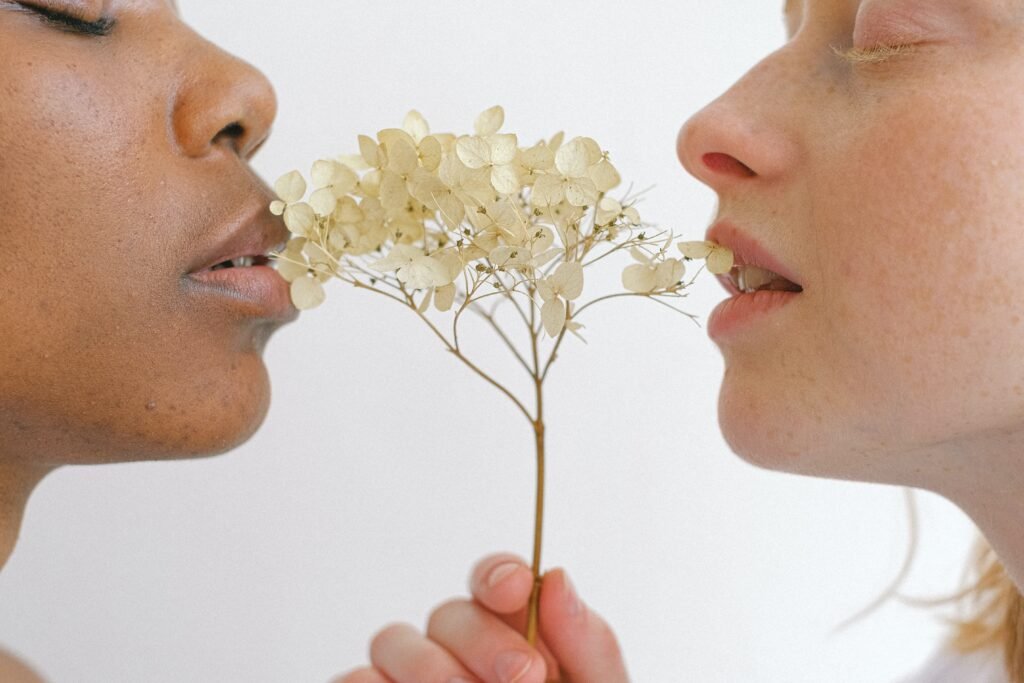 A couple is facing each other while smelling a small tree in between them.