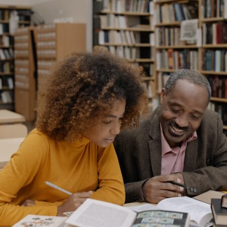 An African man with his daughter in the library, sharing ideas from a book on personal growth and development