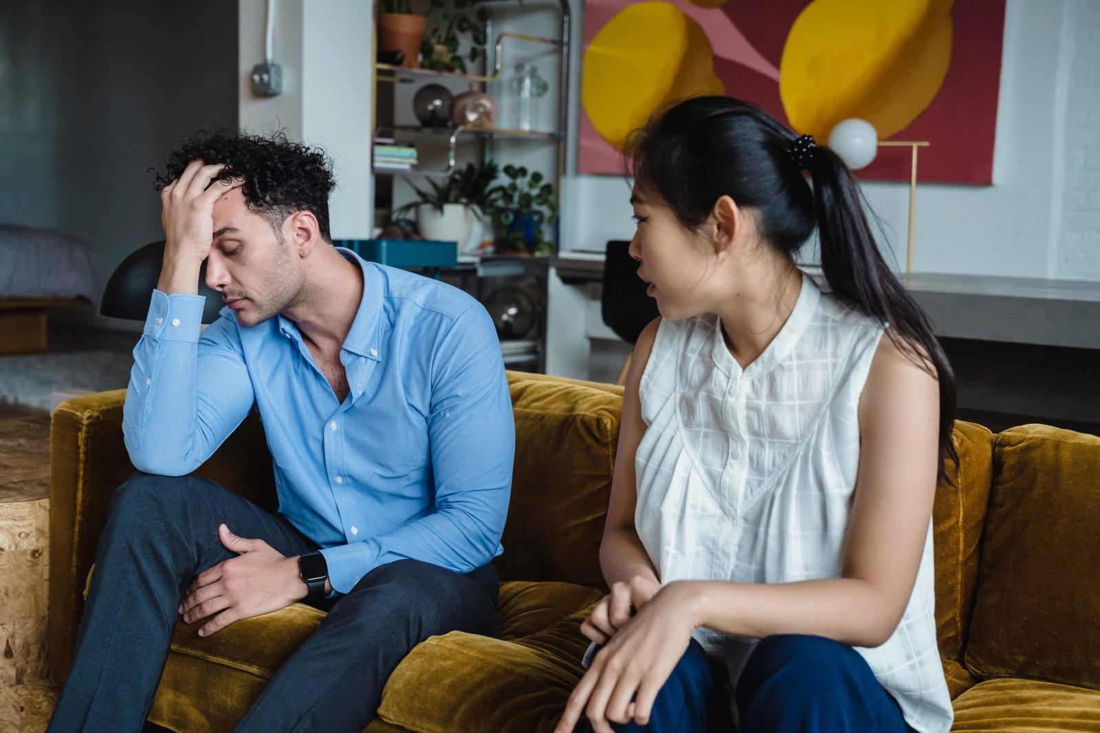 An Asian couple seated on the couch facing the roommate syndrome as they discuss their conflicts. The husband is feeling dejected with his right hand on his head.