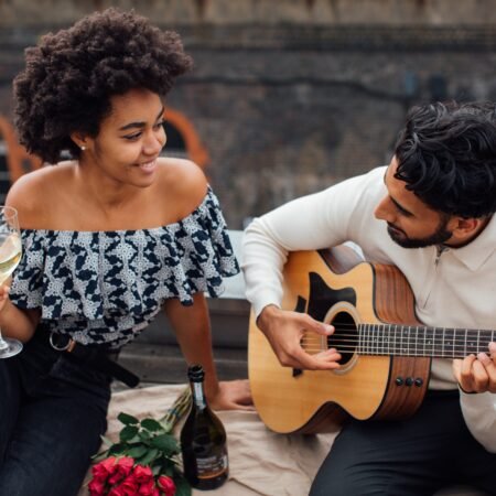 A young couple enjoy each other's company. The lady is sipping a glass of wine while her husband is playing their favourite tunes on guitar. They're dispelling some of the relationship myths.