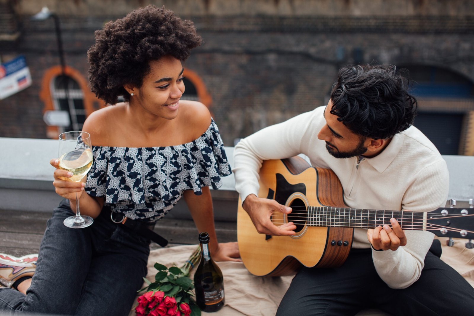 A young couple enjoy each other's company. The lady is sipping a glass of wine while her husband is playing their favourite tunes on guitar. They're dispelling some of the relationship myths.