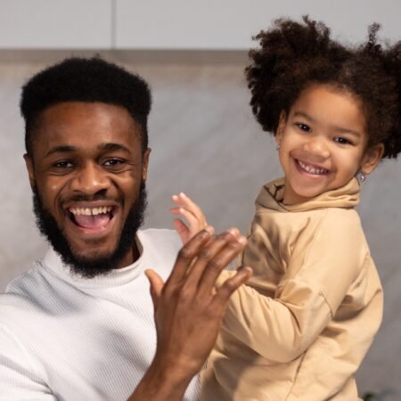 A happy African dad and his pretty daughter looking straight to the camera, the former content of being a good father.