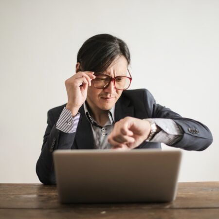 An executive checking the time on his watch while working on his computer. He wary of the tough love of his partner for his workaholism.