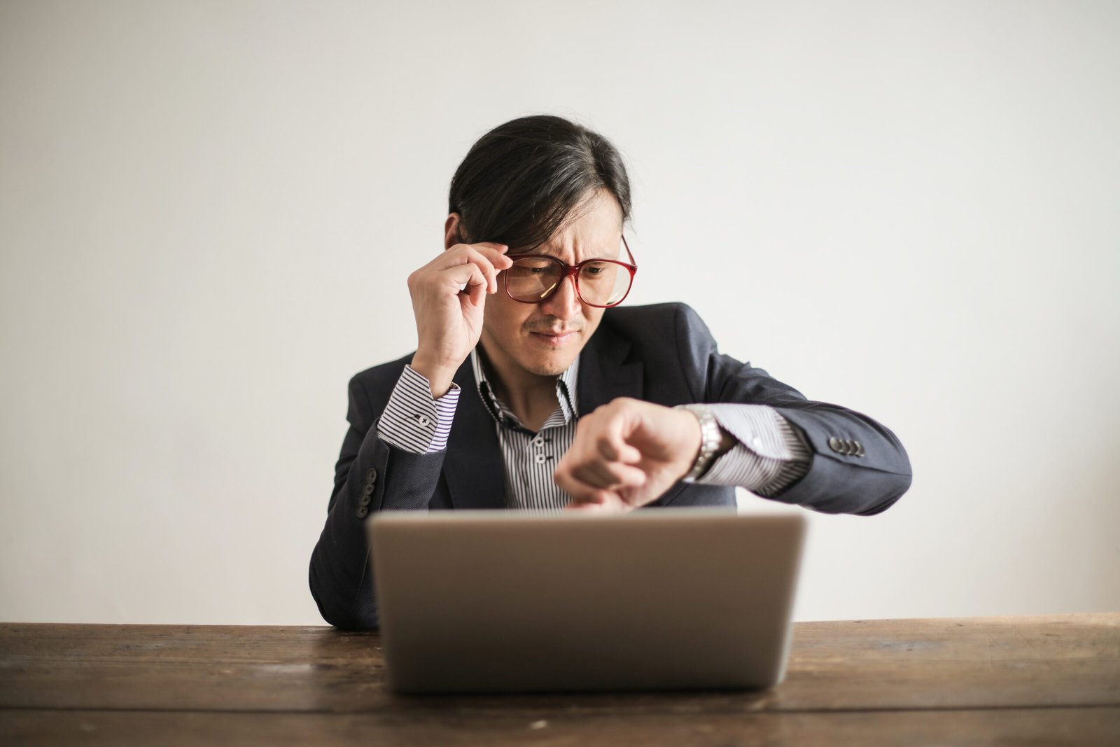 An executive checking the time on his watch while working on his computer. He wary of the tough love of his partner for his workaholism.