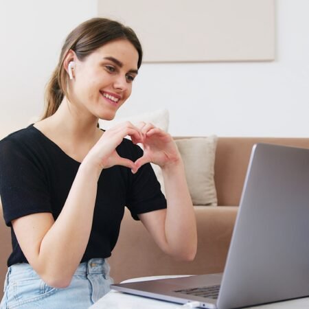 A lady on a video call with her fiancé, displaying the love sign while pondering "is love at first sight real?"