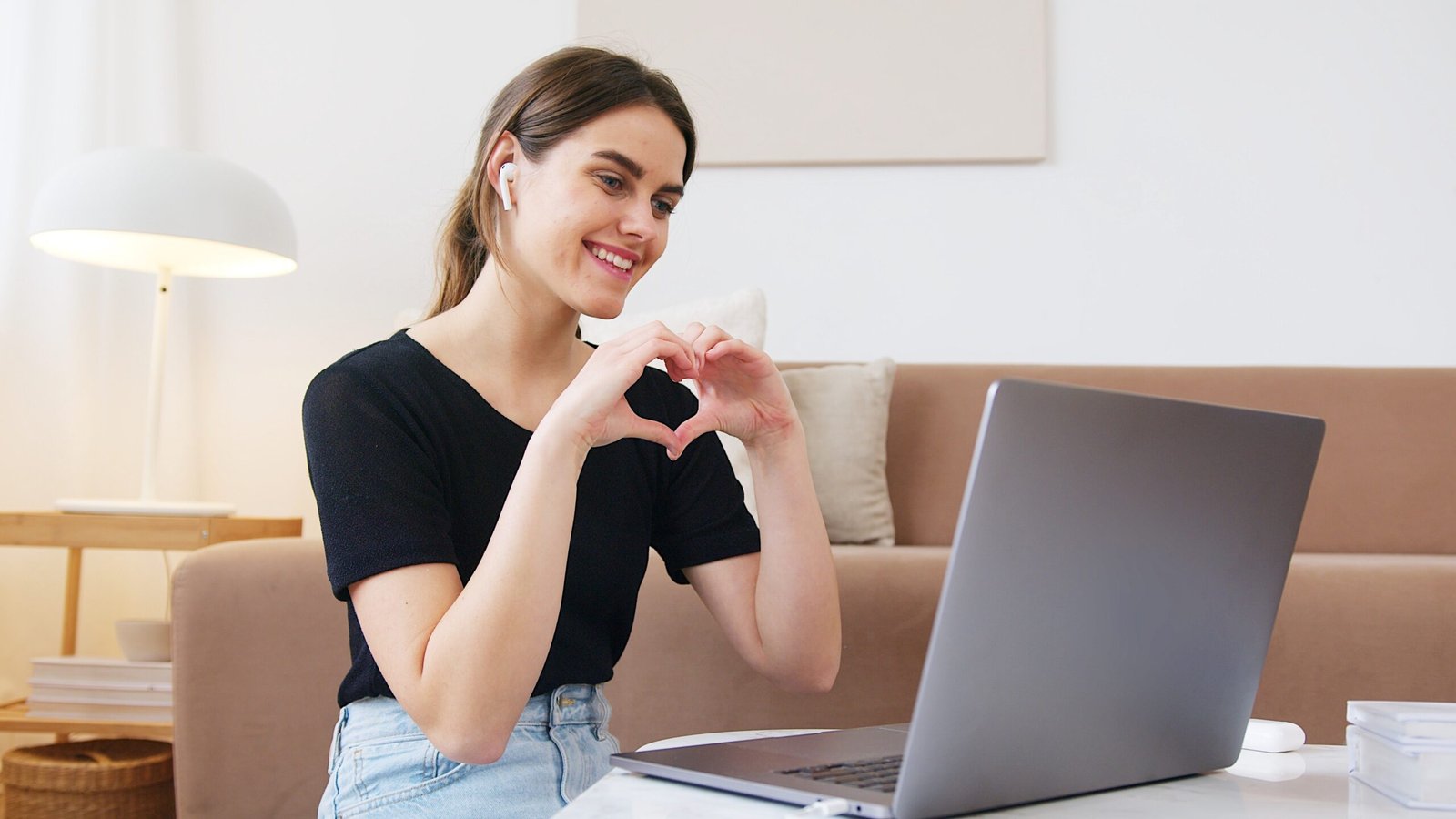 A lady on a video call with her fiancé, displaying the love sign while pondering "is love at first sight real?"