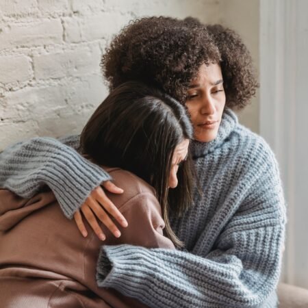 Two Black American sisters are leaning on each other's shoulders as they mourn a family member's loss.