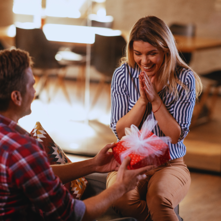 A husband kneeling and presenting an anniversary gift to his surprised wife cognizant of happy wife happy life mantra.