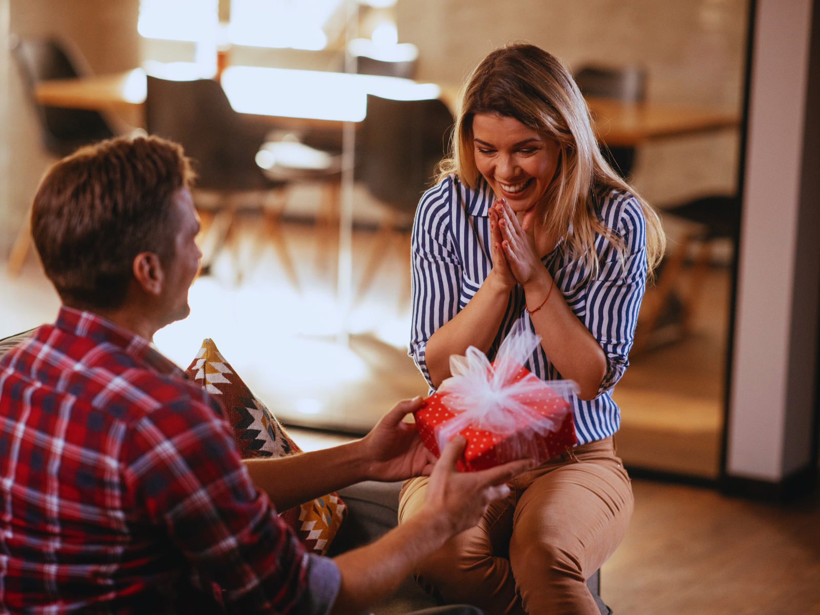 A husband kneeling and presenting an anniversary gift to his surprised wife cognizant of happy wife happy life mantra.